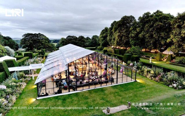 Exterior de una carpa tipo invernadero para un evento en el jardín, con paredes de cristal e iluminación nocturna