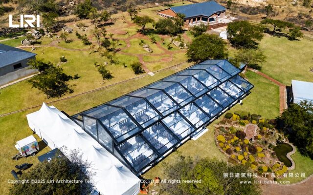 Vista aérea de una carpa tipo invernadero para eventos al aire libre, con techo transparente y entorno ajardinado